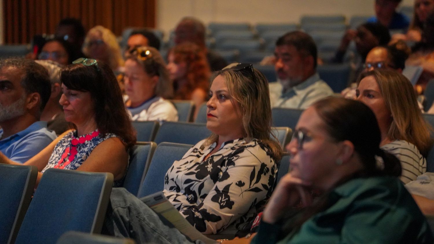 Diverse audience members seated in blue theater chairs during presentation.