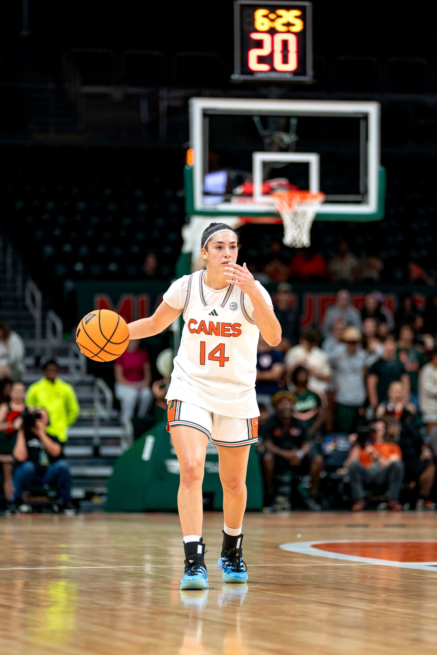 Basketball player dribbles on court wearing white uniform with number 14.
