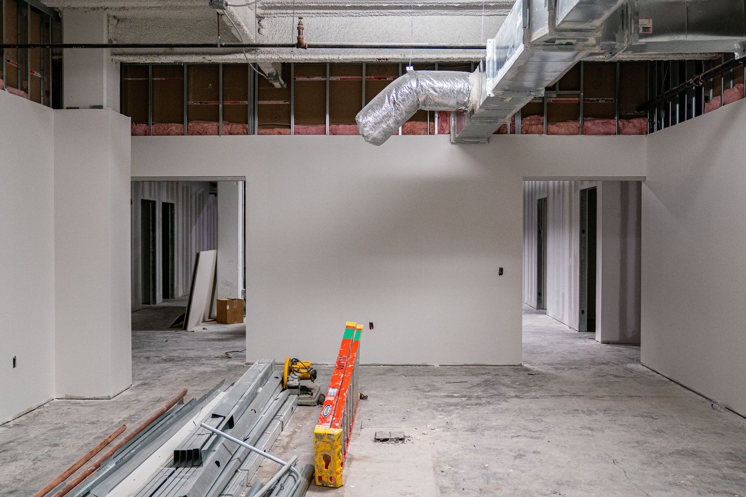 Large empty warehouse space with white walls and construction materials scattered on floor.