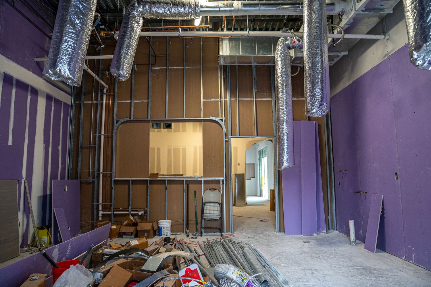 Commercial space with purple walls showing mechanical systems and exposed ceiling during buildout.