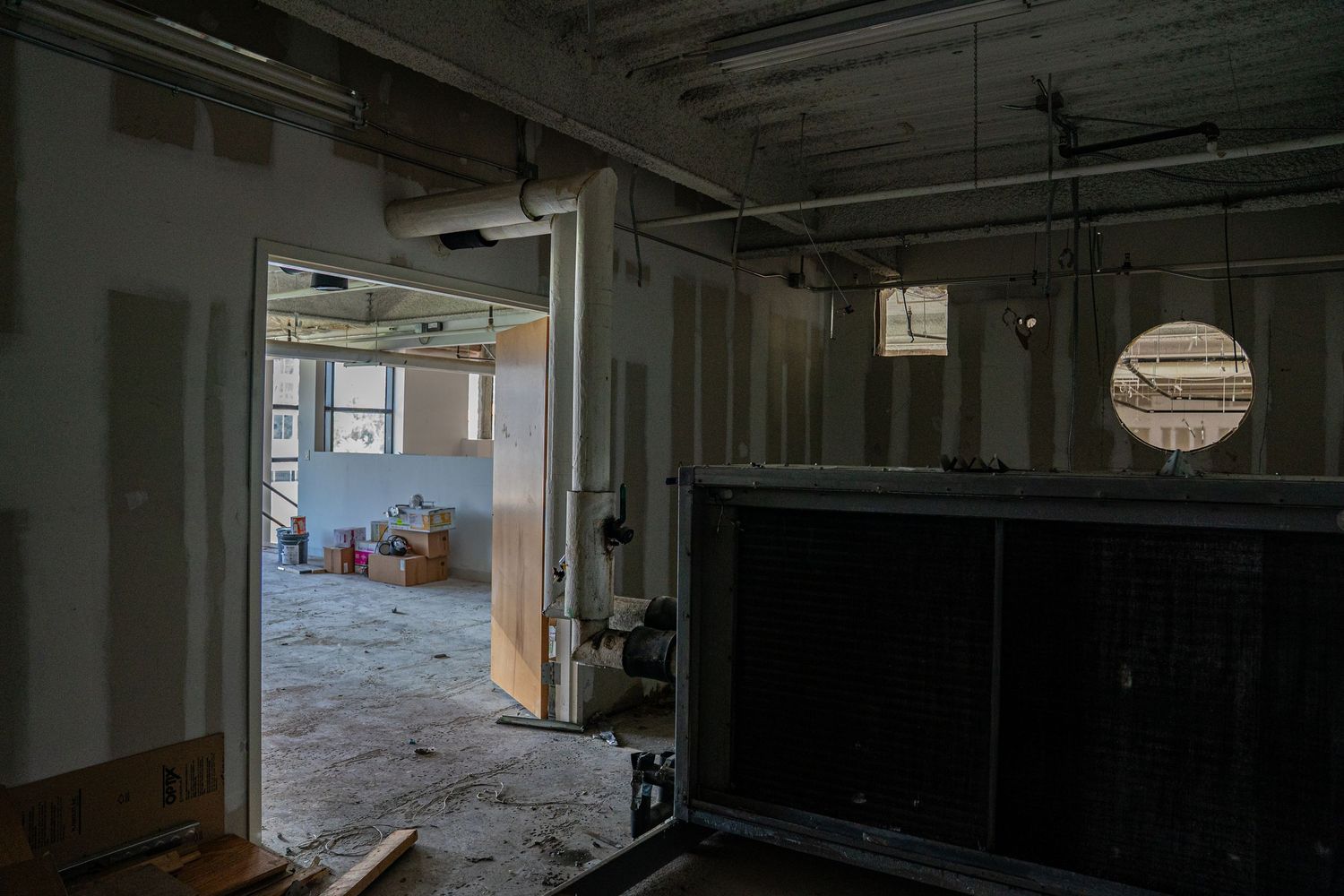 Dark industrial interior with exposed ceiling infrastructure and windows letting in natural light.