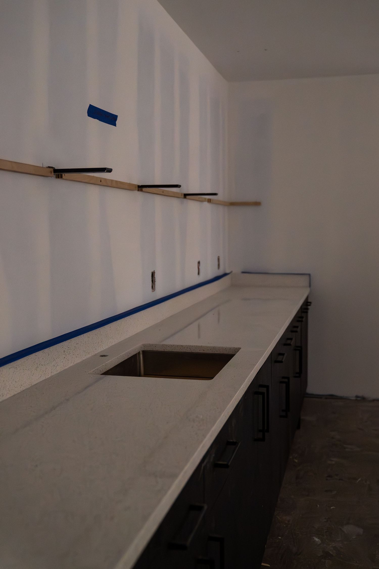 White counter installation in progress with dark base cabinets and blue tape markings.