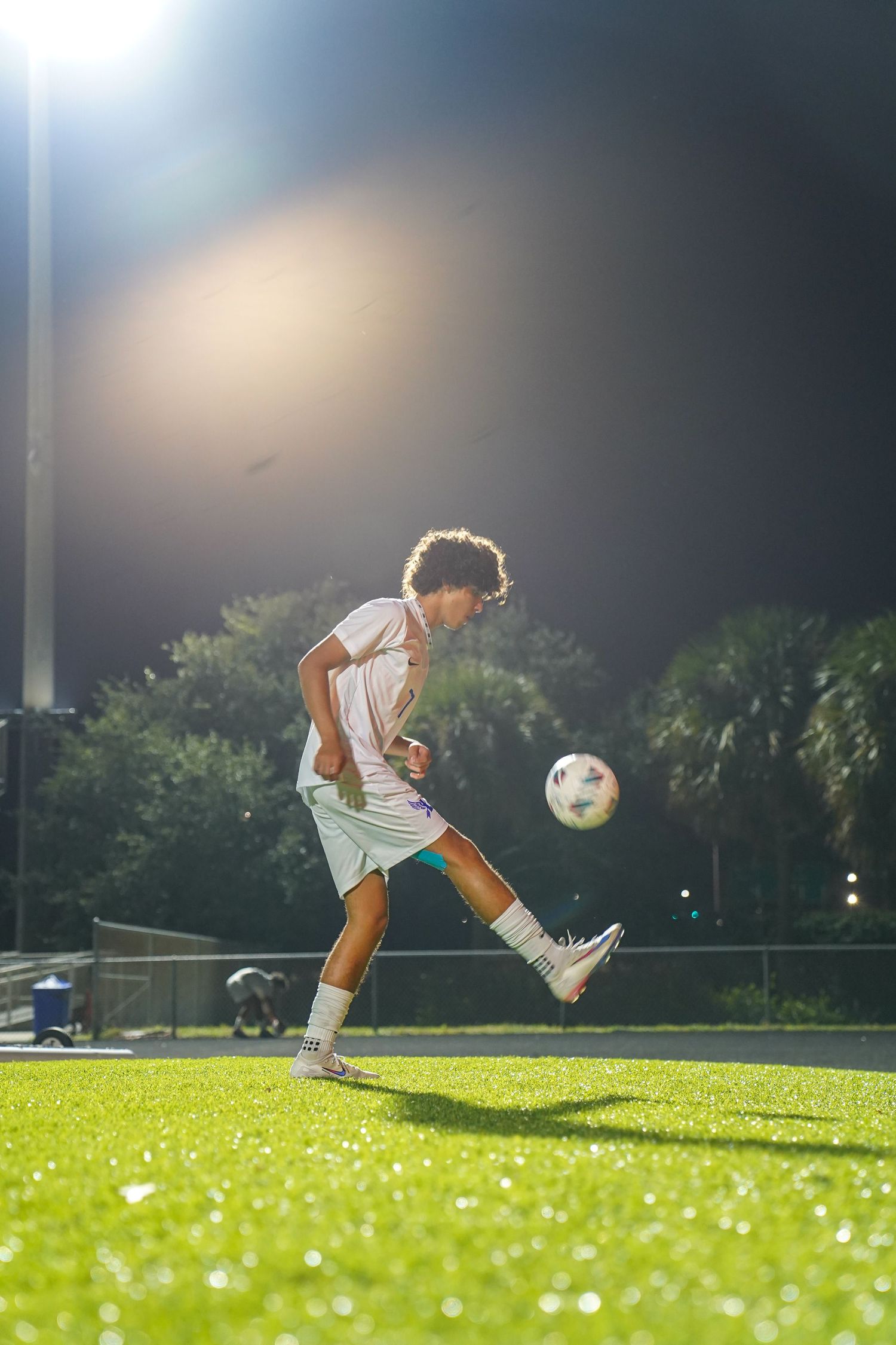 Soccer player practicing ball control drills on a green field at night.