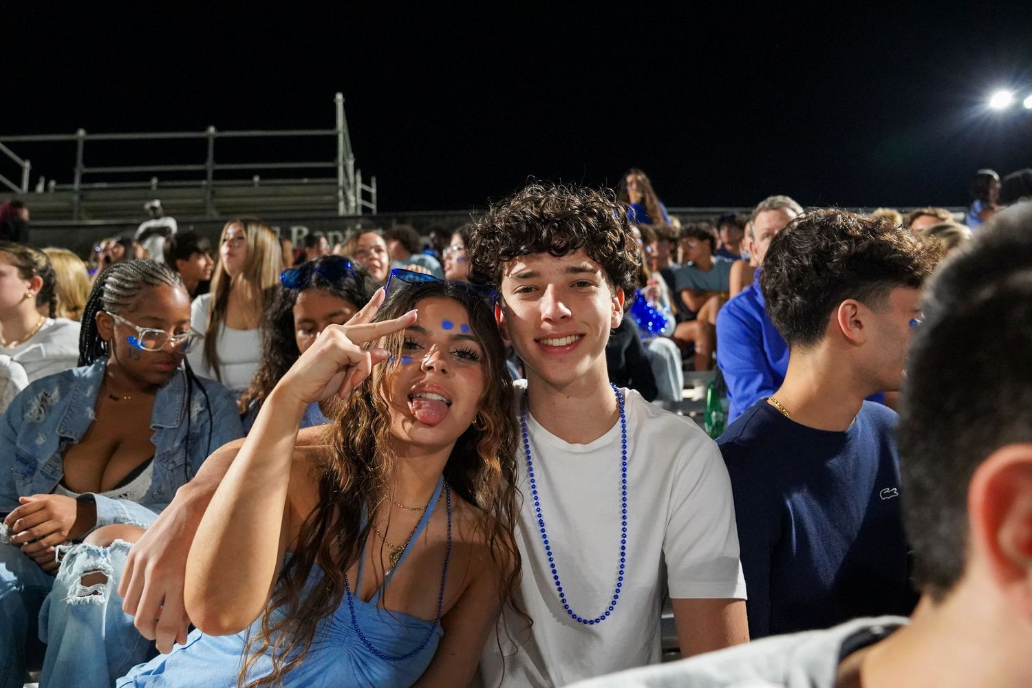Enthusiastic fans in blue and white colors celebrating together at a night game.