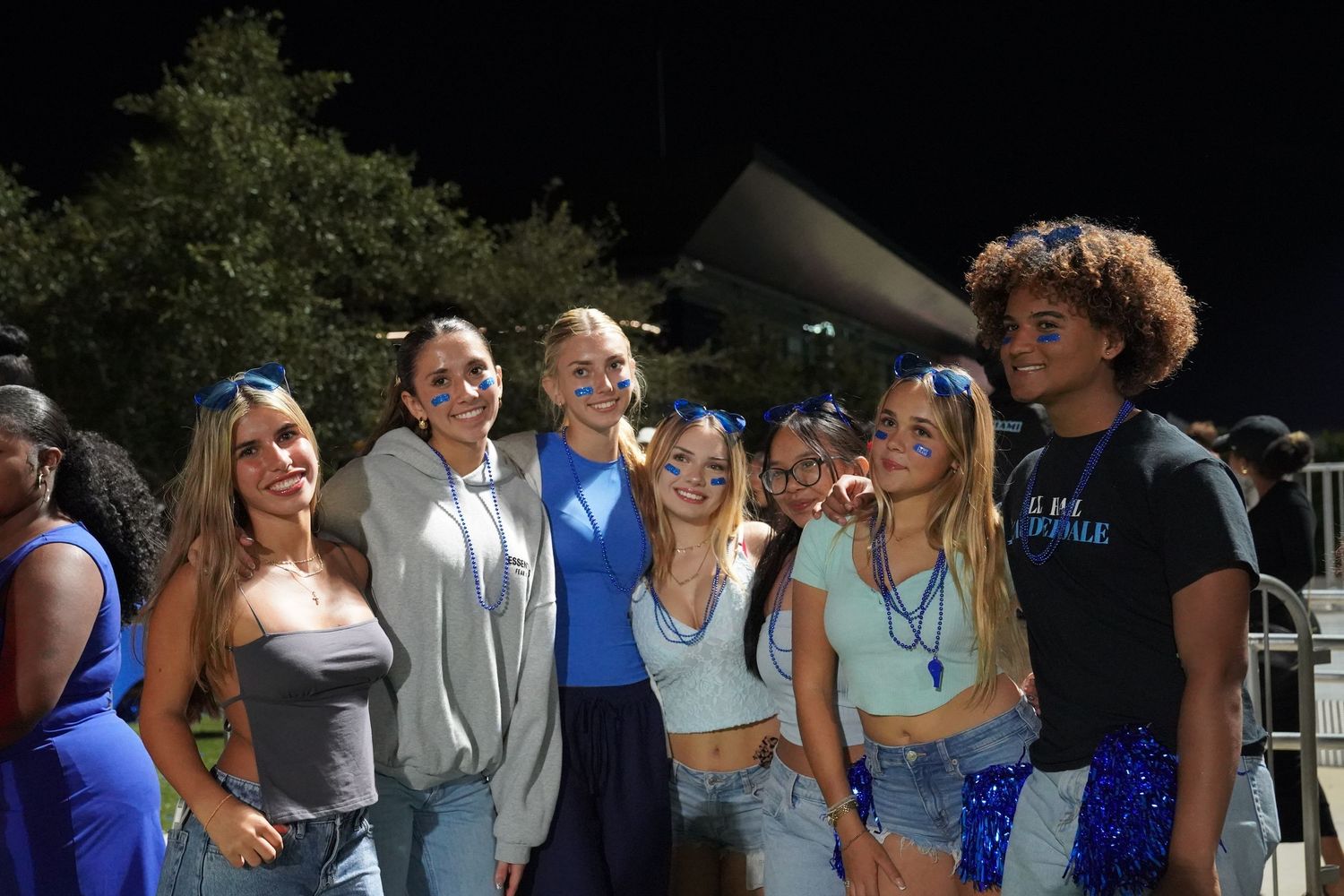 Students gather in groups under stadium lights for an outdoor evening celebration.