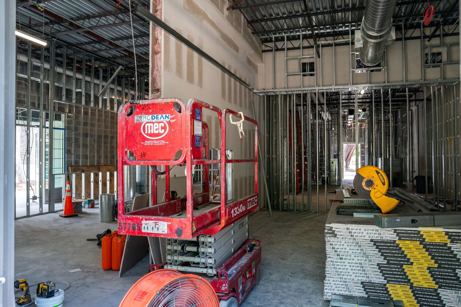 Construction site interior with metal framing and red equipment visible throughout space.
