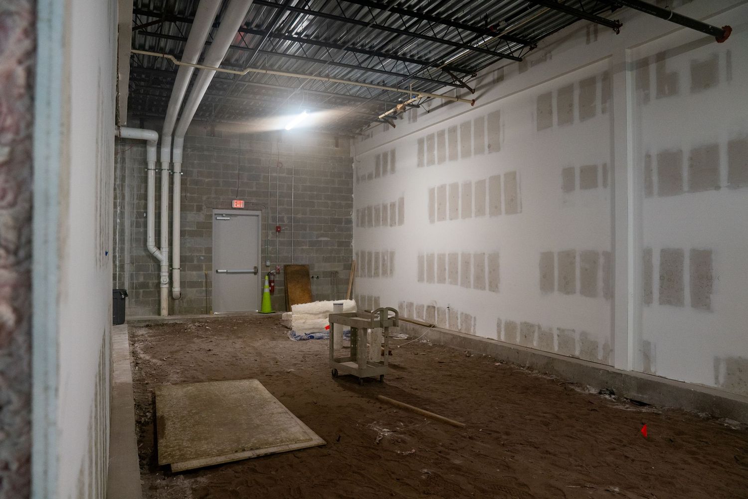 Construction site interior showing drywall installation and exposed utilities in commercial space.