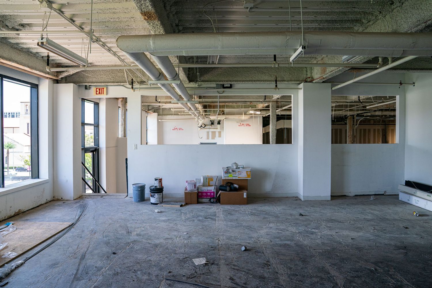 Wide angle view of empty commercial floor space with concrete floors and large windows.