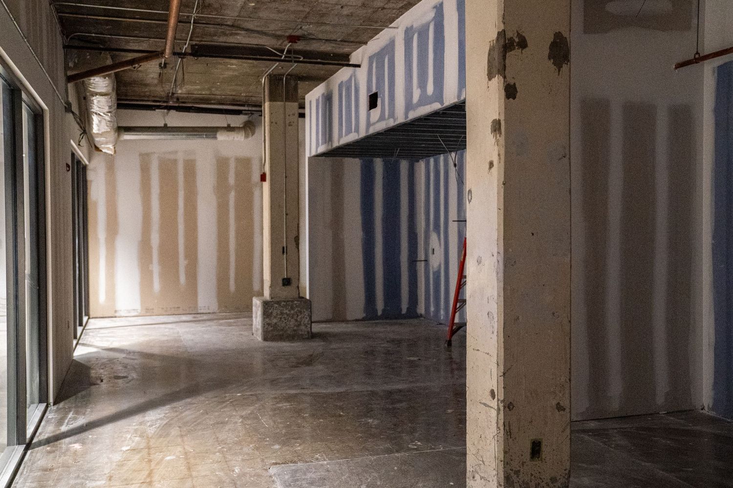 Long corridor view of commercial space under construction with drywall and exposed ceiling.