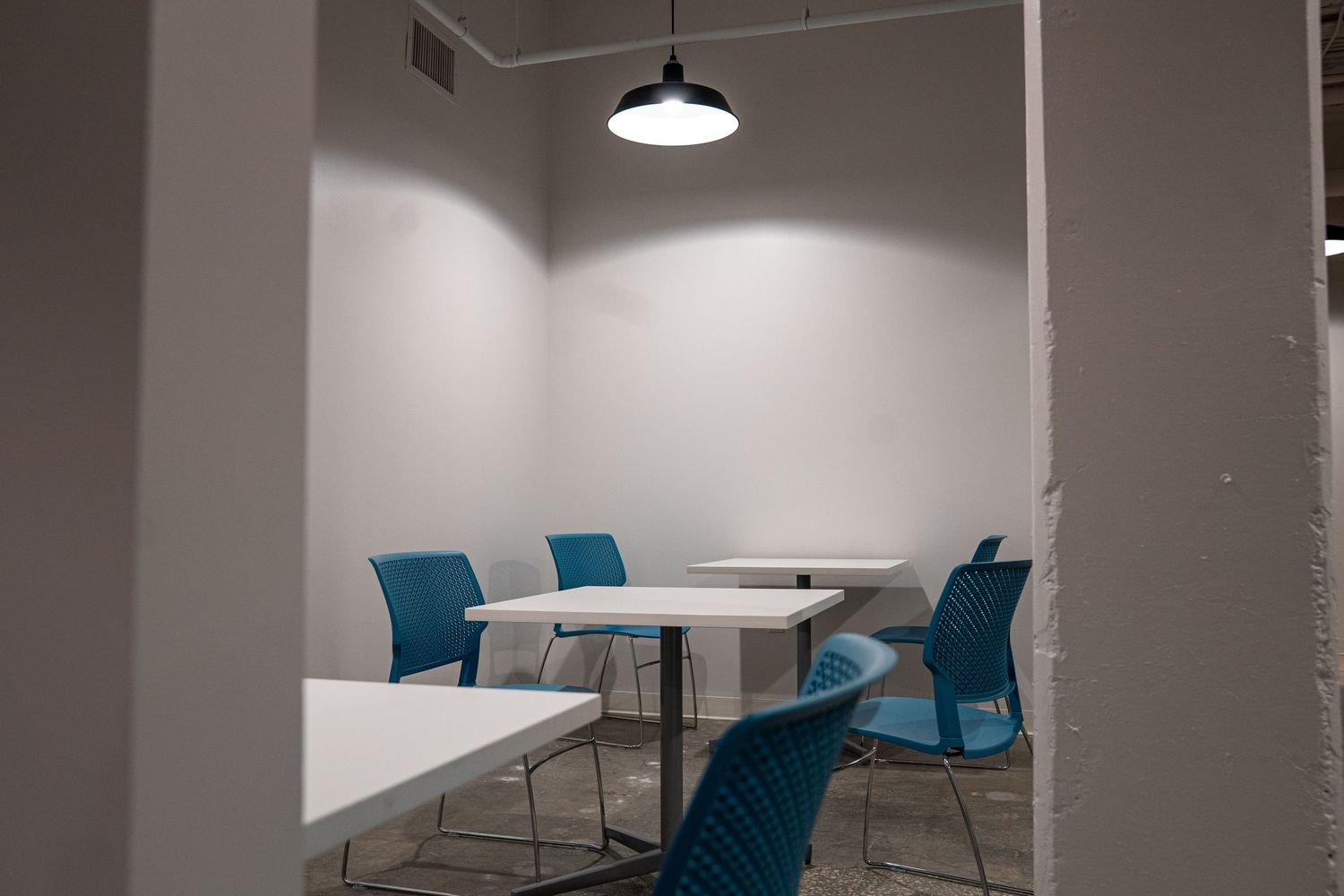 Modern office break room with blue chairs and pendant lighting.