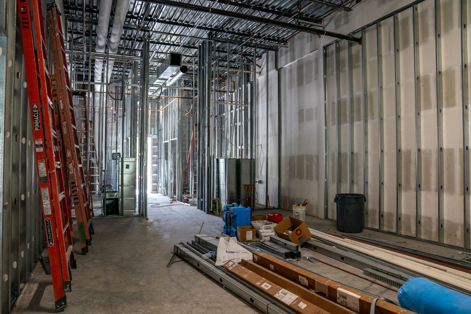 Interior construction progress showing metal stud framing and exposed ceiling in large commercial space.