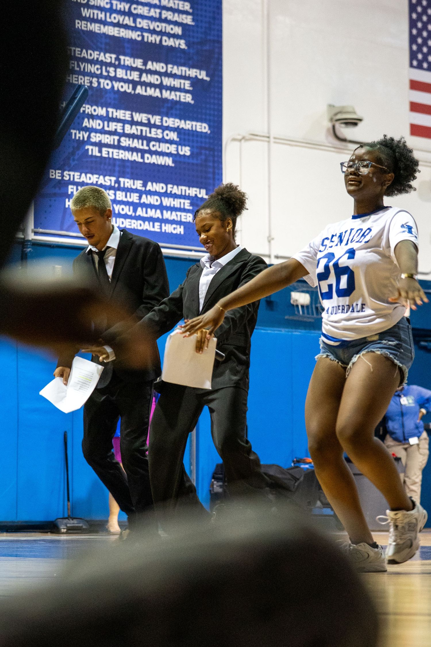 Students in graduation gowns celebrate at a Fort Lauderdale high school pep rally in a gymnasium.