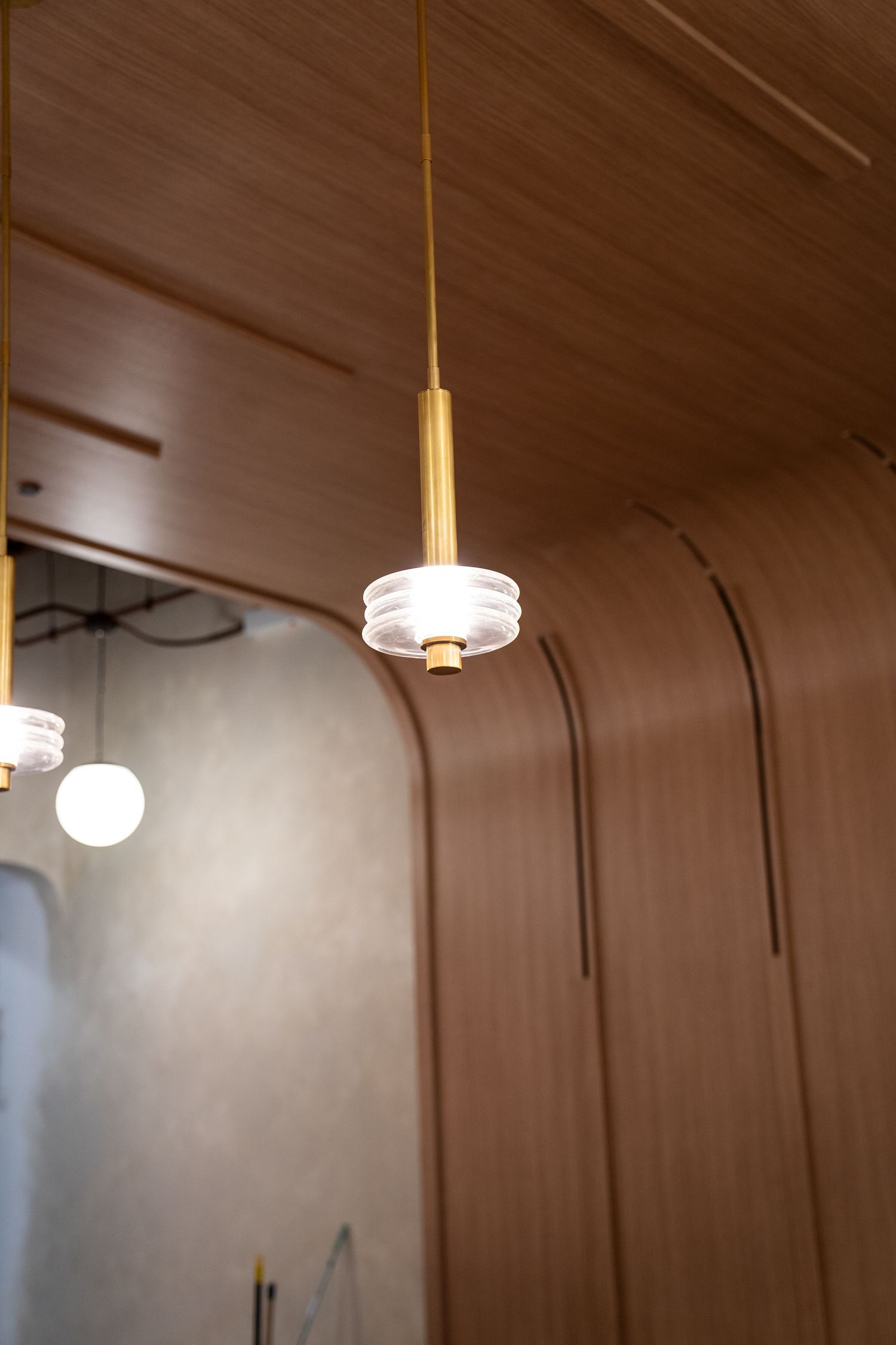 Modern pendant light fixture with brass hardware and frosted glass shade hanging from a wood-paneled ceiling.