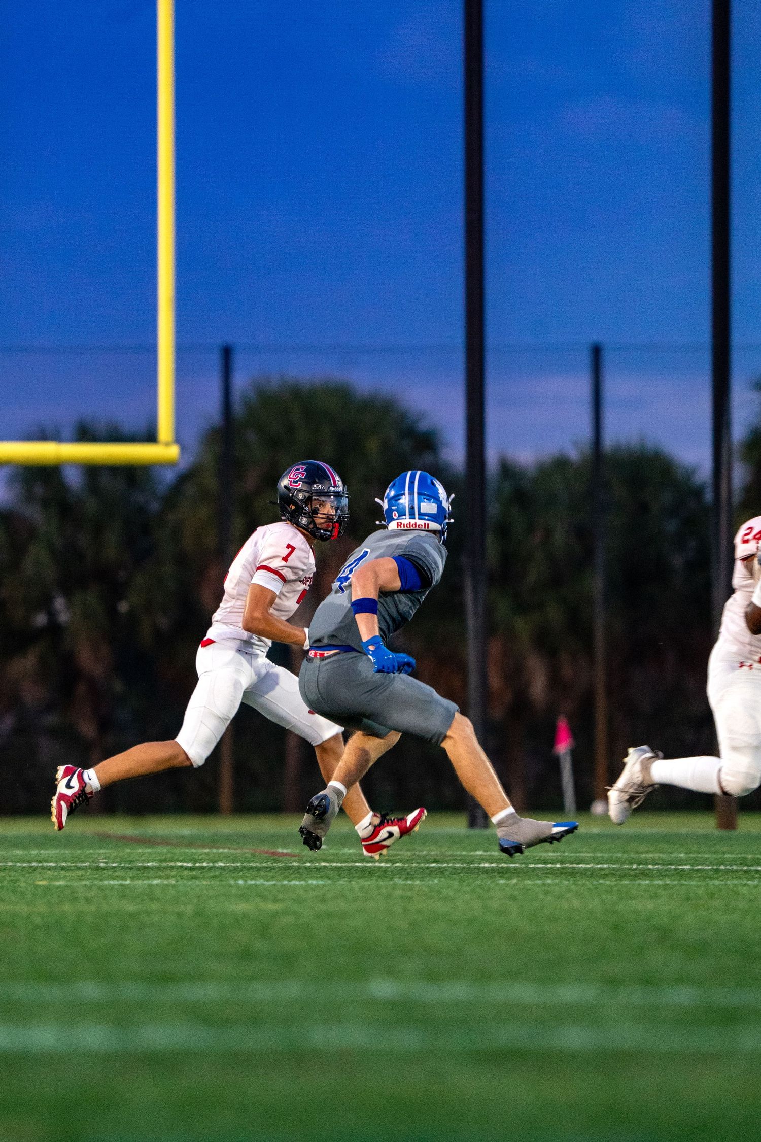 Football players diving for tackle on grass field near goal post.