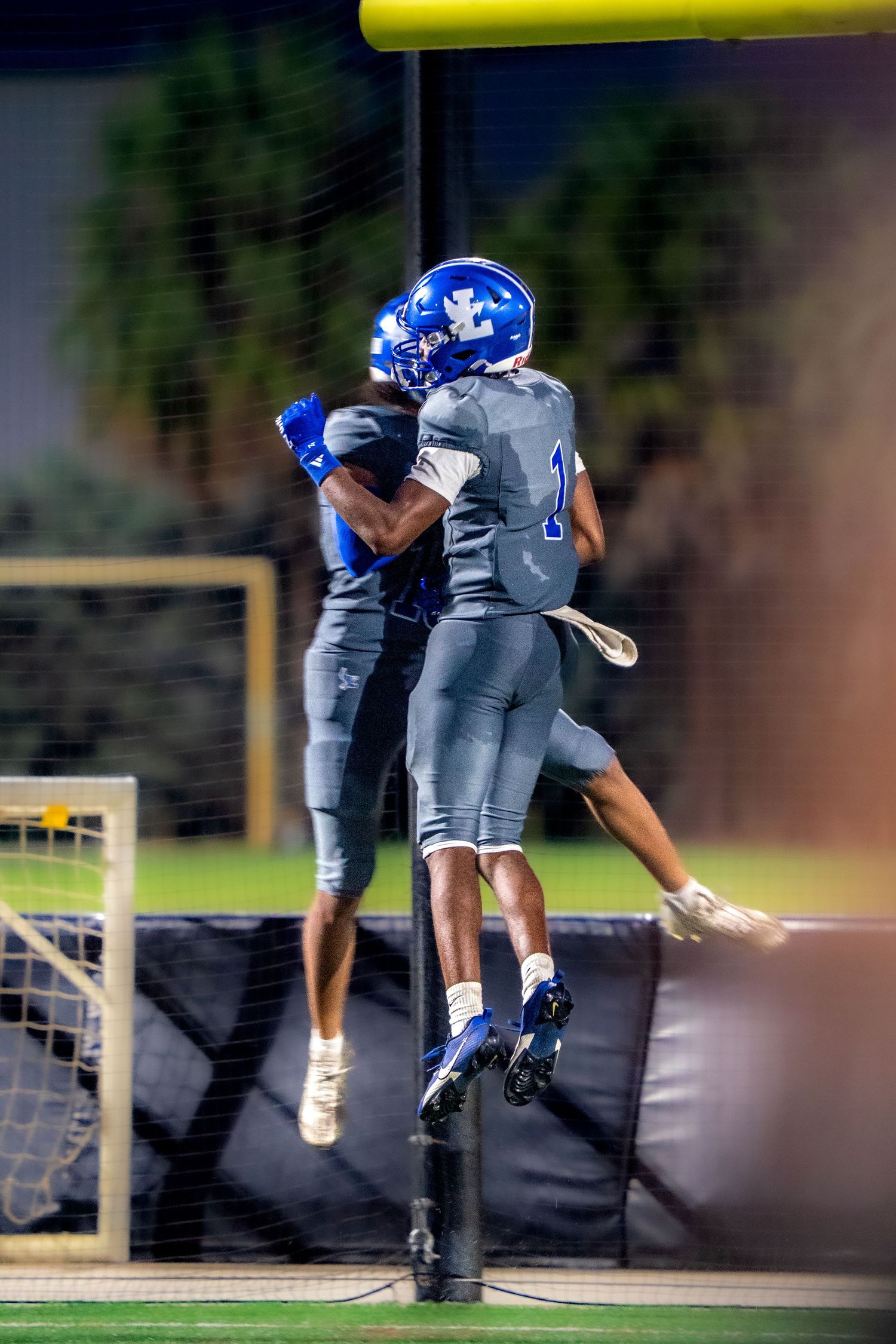Football players in blue uniforms celebrating with mid-air celebration.