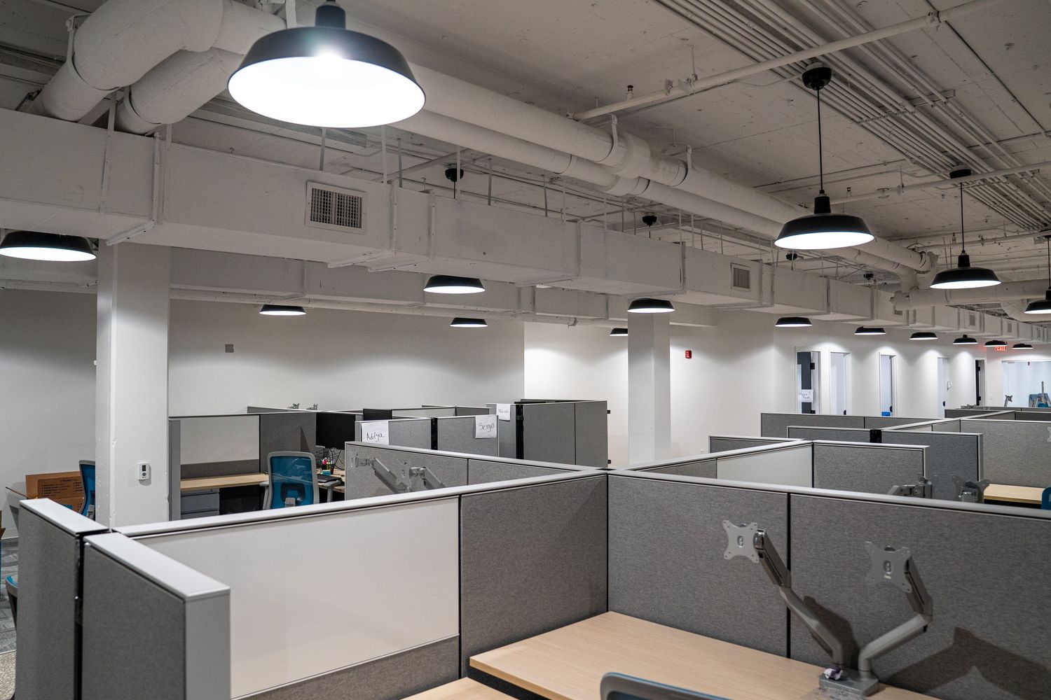Corporate office space with industrial ceiling design, cubicle partitions, and modern workstations.