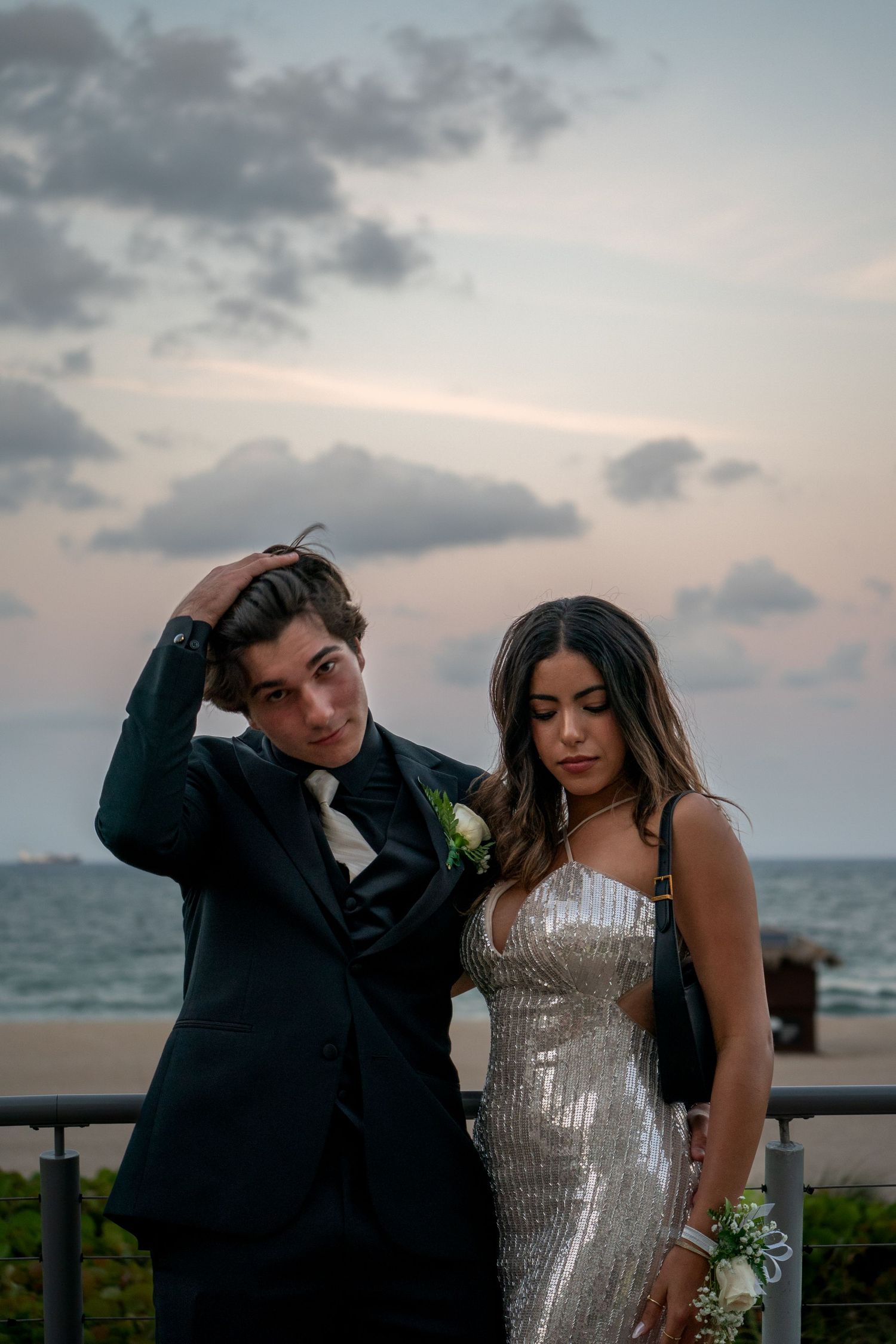 Couple poses for romantic sunset photos by ocean railing.