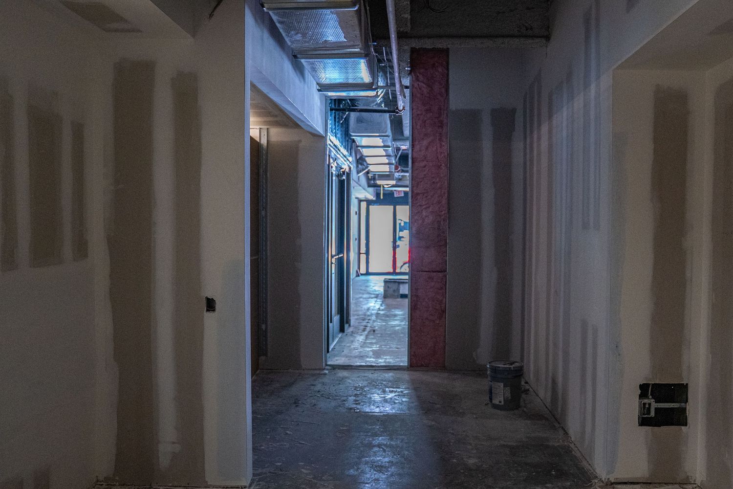 Dark hallway under construction with exposed utilities and white drywall.