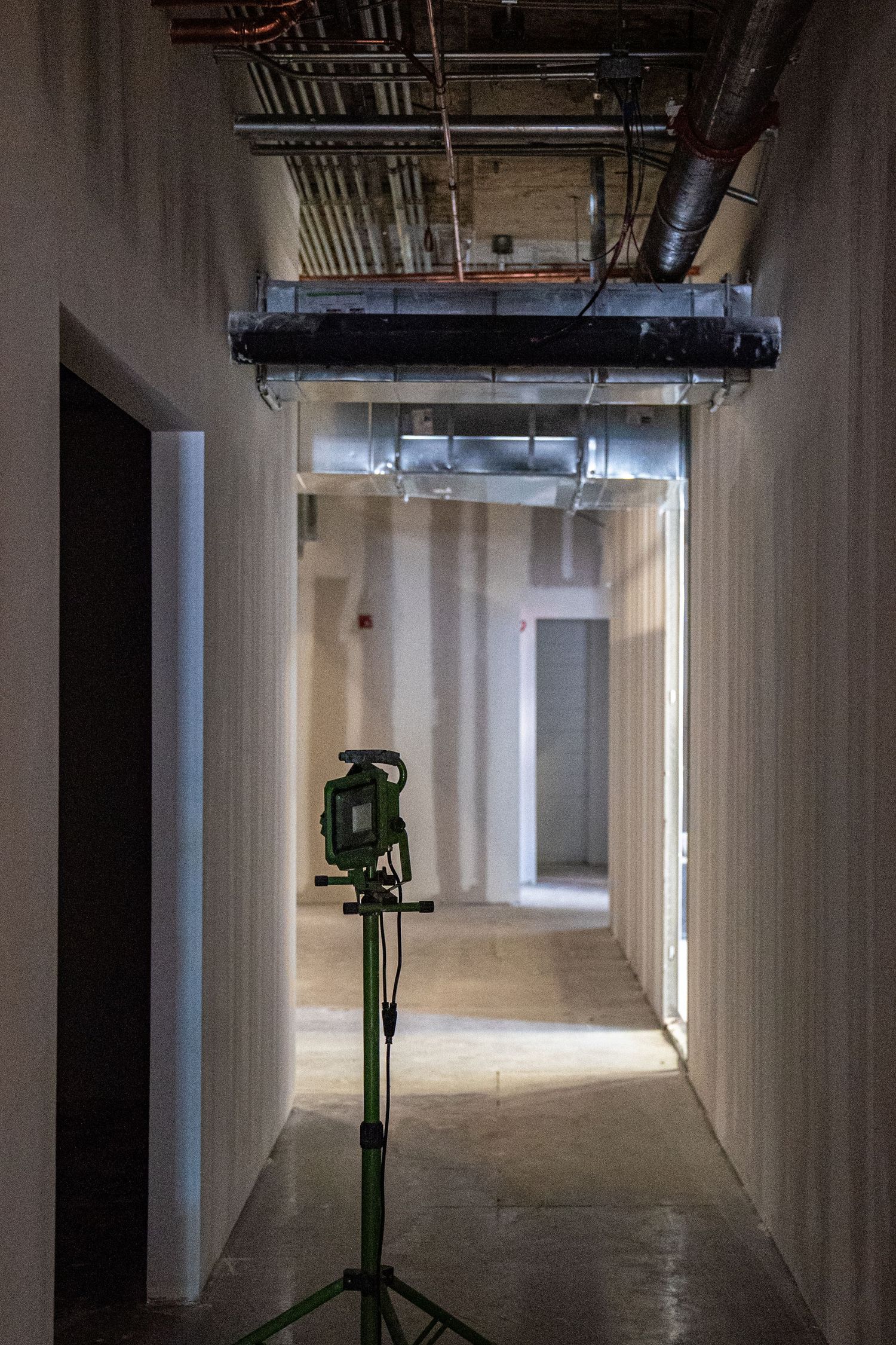 Long empty hallway under construction with exposed ceiling and bright lighting at the end.