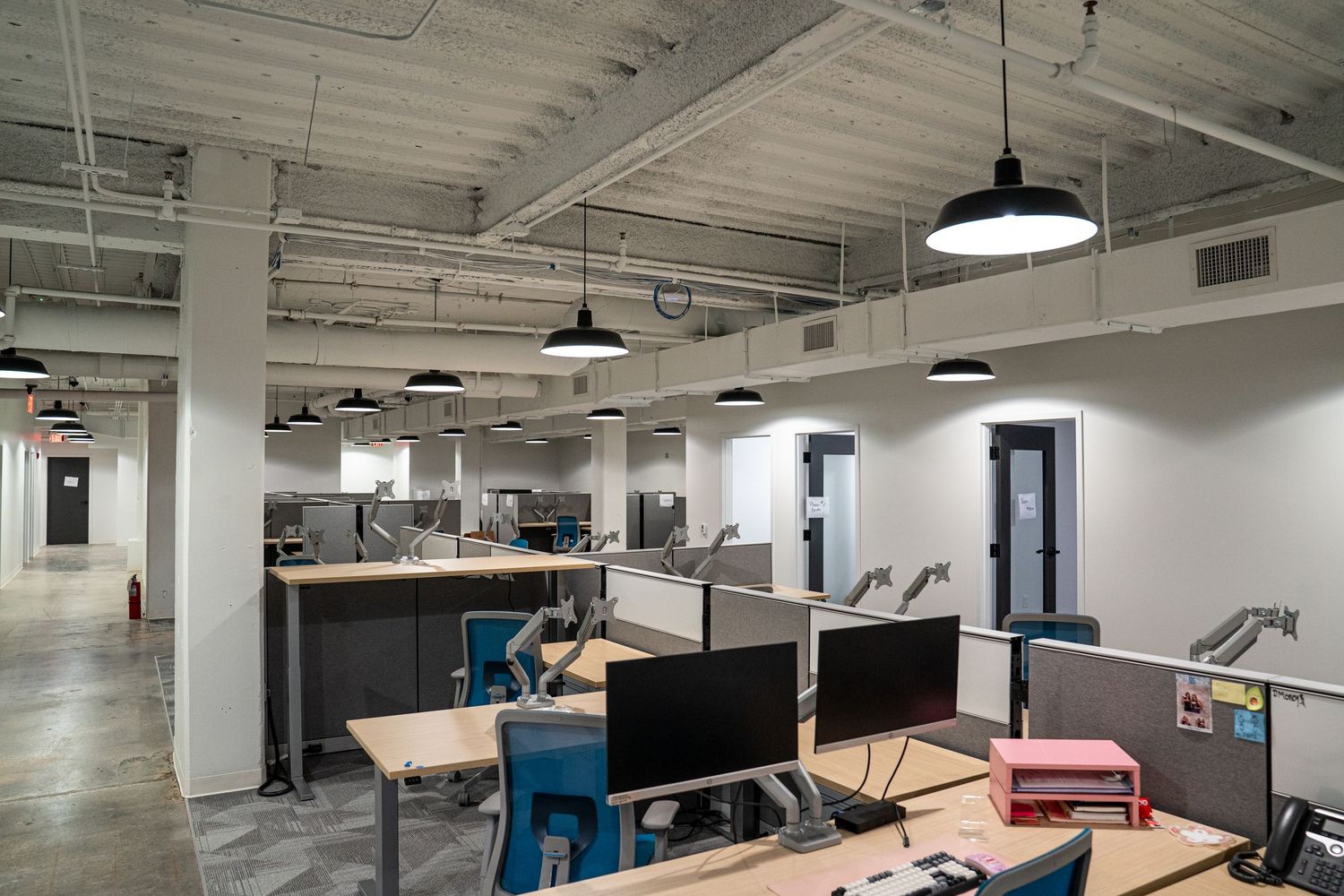 Spacious open plan office with exposed ductwork, pendant lighting, and modular workstations.