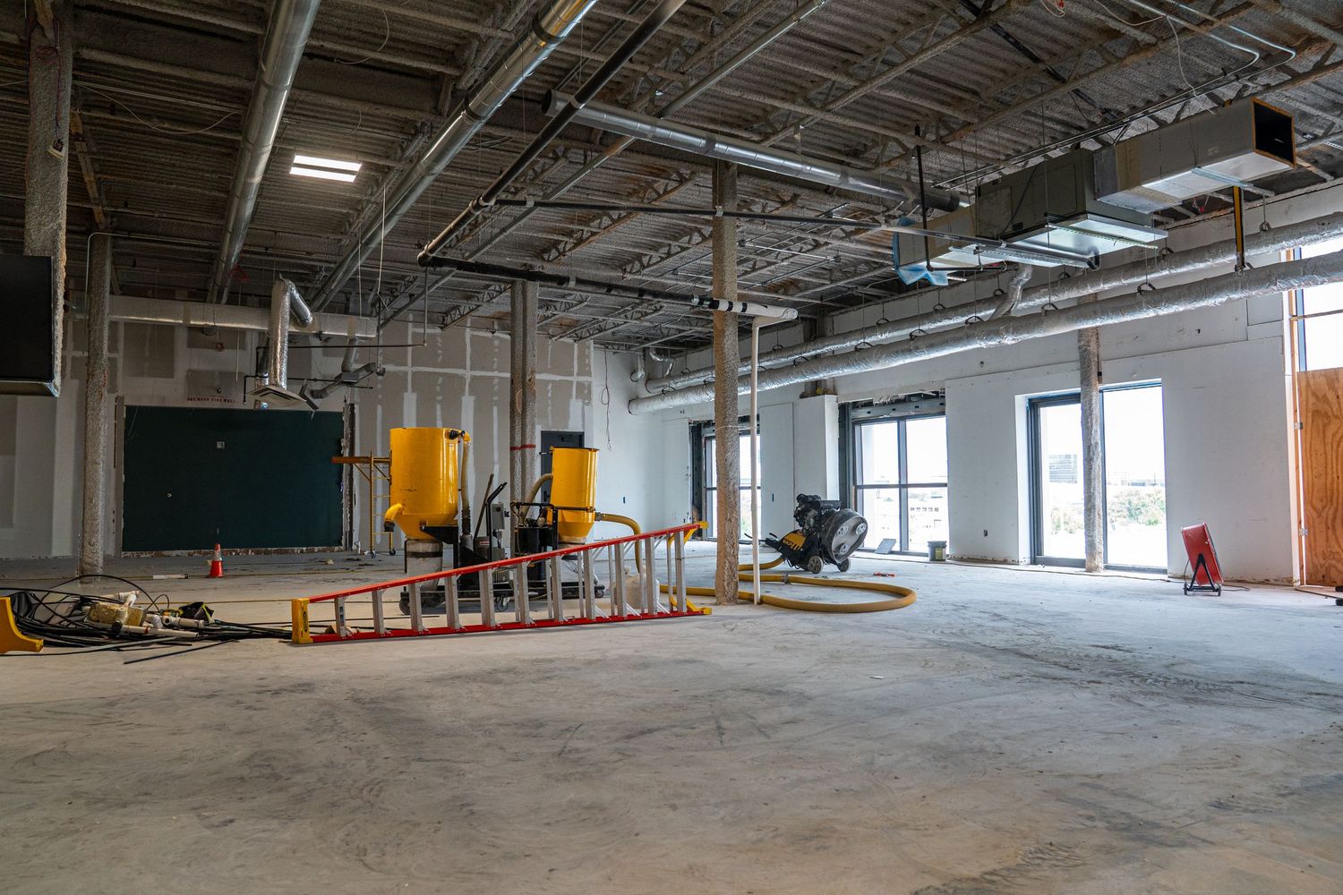Expansive industrial warehouse space under renovation with concrete floors and exposed utilities.