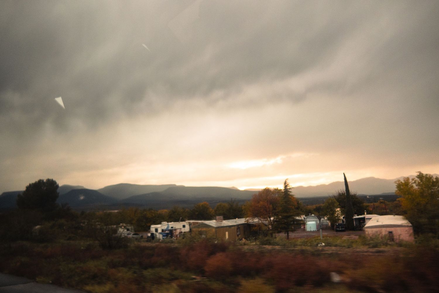 Rural landscape with mountains and scattered buildings under moody evening sky.