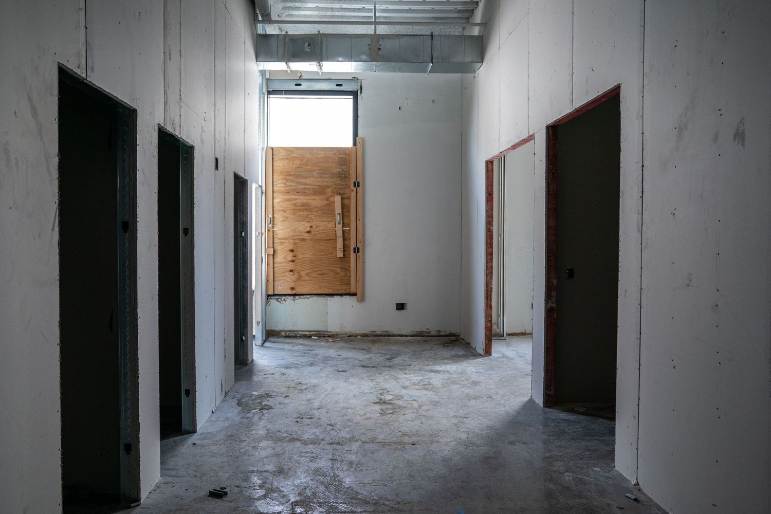 A stark hallway with dark doors and a wooden board covering an opening at the end.