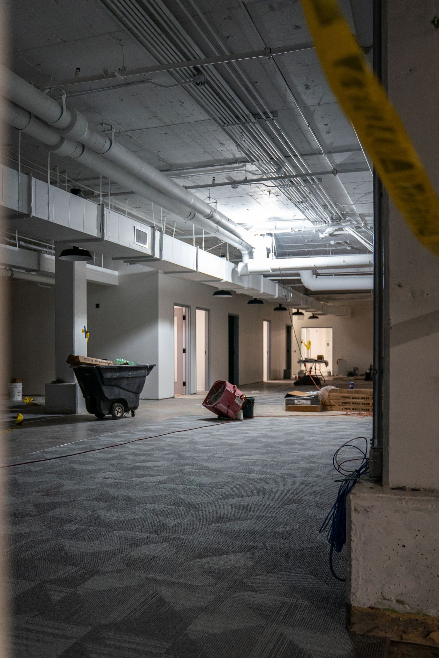 Industrial hallway under construction with exposed ceiling utilities and scattered building materials.