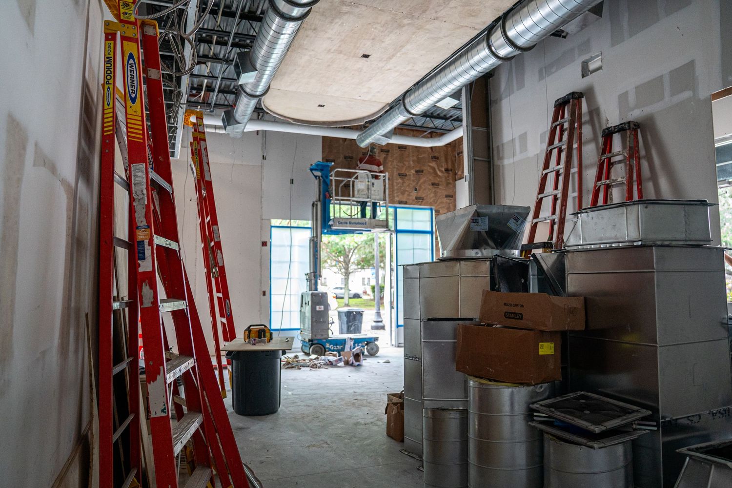 Construction site interior showing red ladders and exposed ceiling with ductwork during renovation.