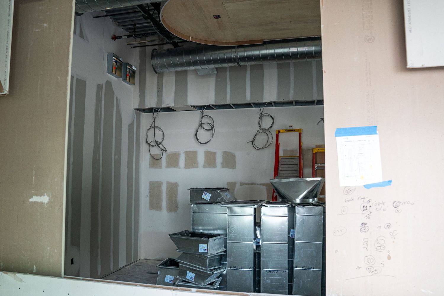 Commercial construction site showing exposed ceiling with ductwork and metal framing in progress.