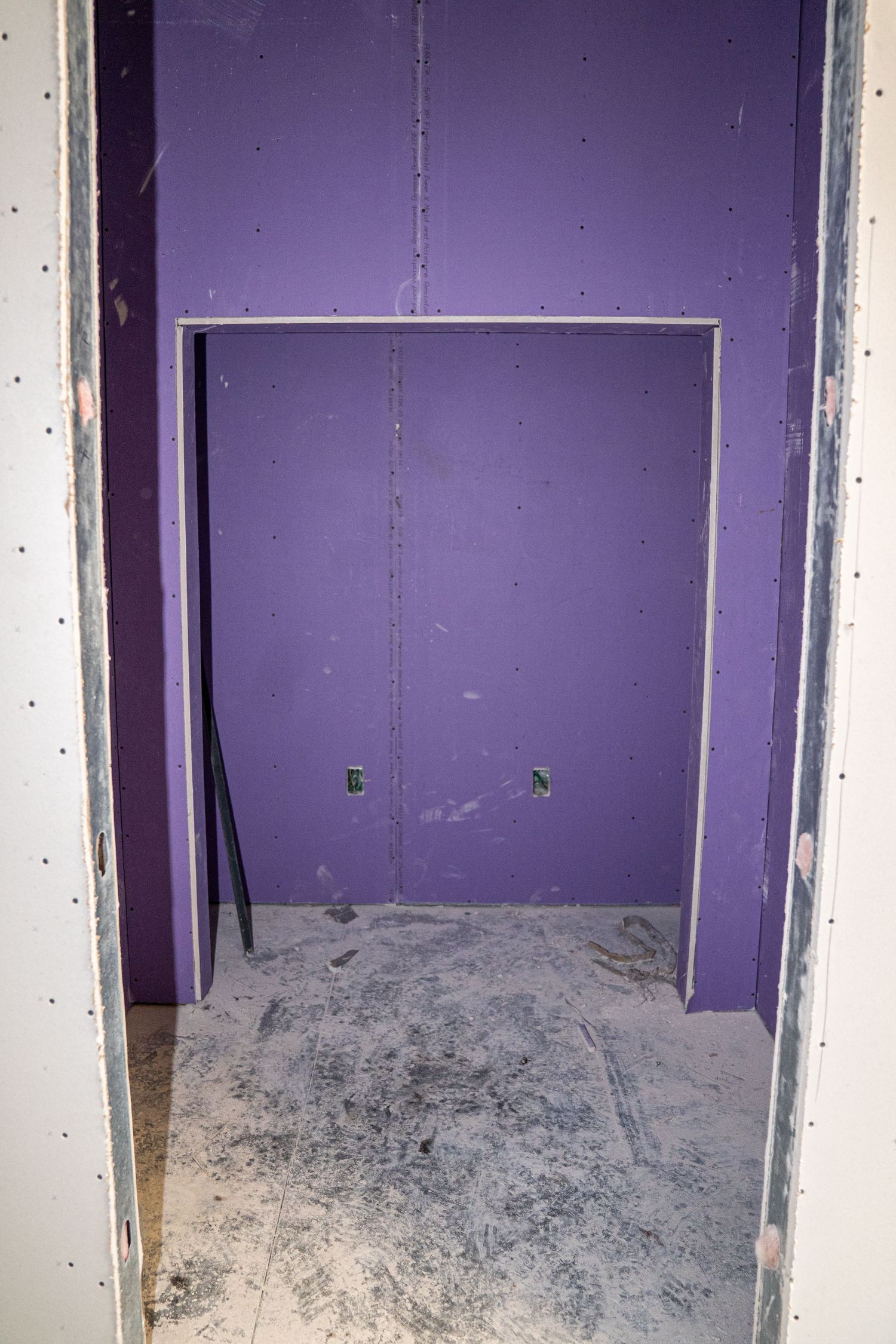 Interior view of an empty room with purple painted walls and exposed concrete floor during construction.