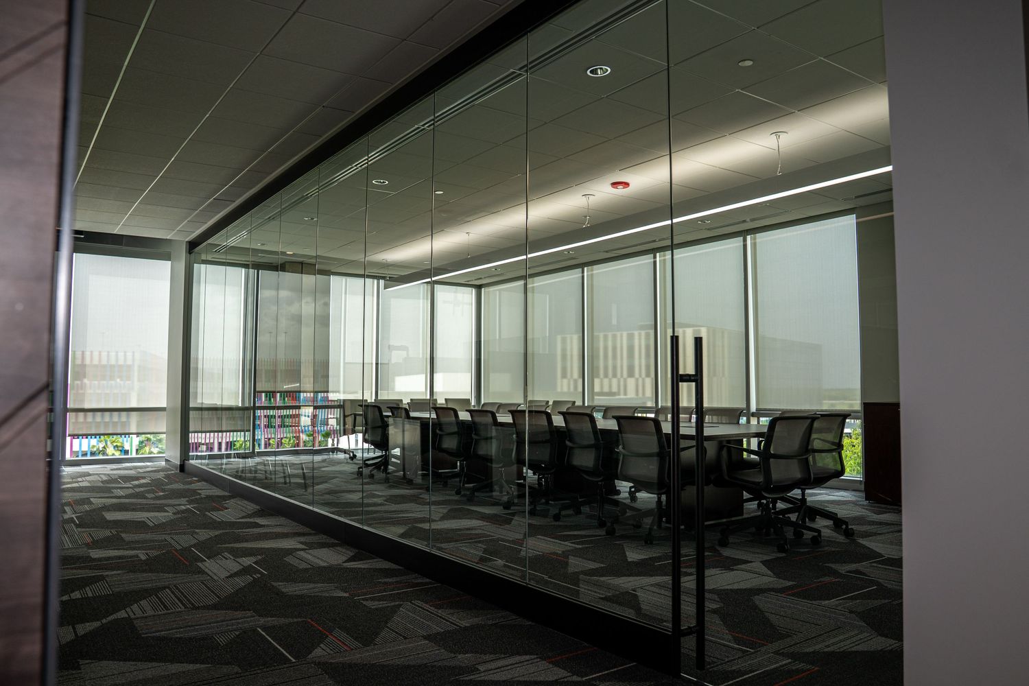 Corporate meeting area with floor-to-ceiling windows, dark office chairs, and geometric carpet design.