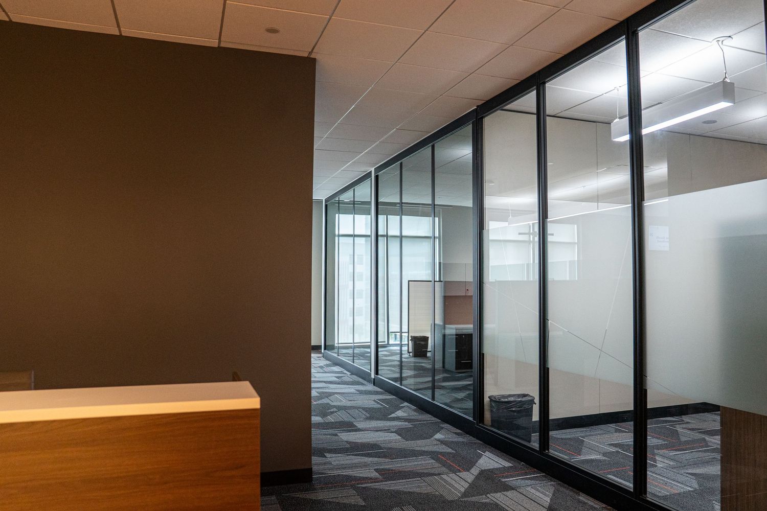 Minimalist office hallway with wooden reception counter, glass walls, and geometric patterned flooring.