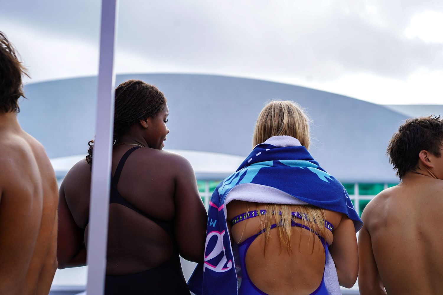 Athletes lined up at a swimming competition starting block preparing to dive into the pool.