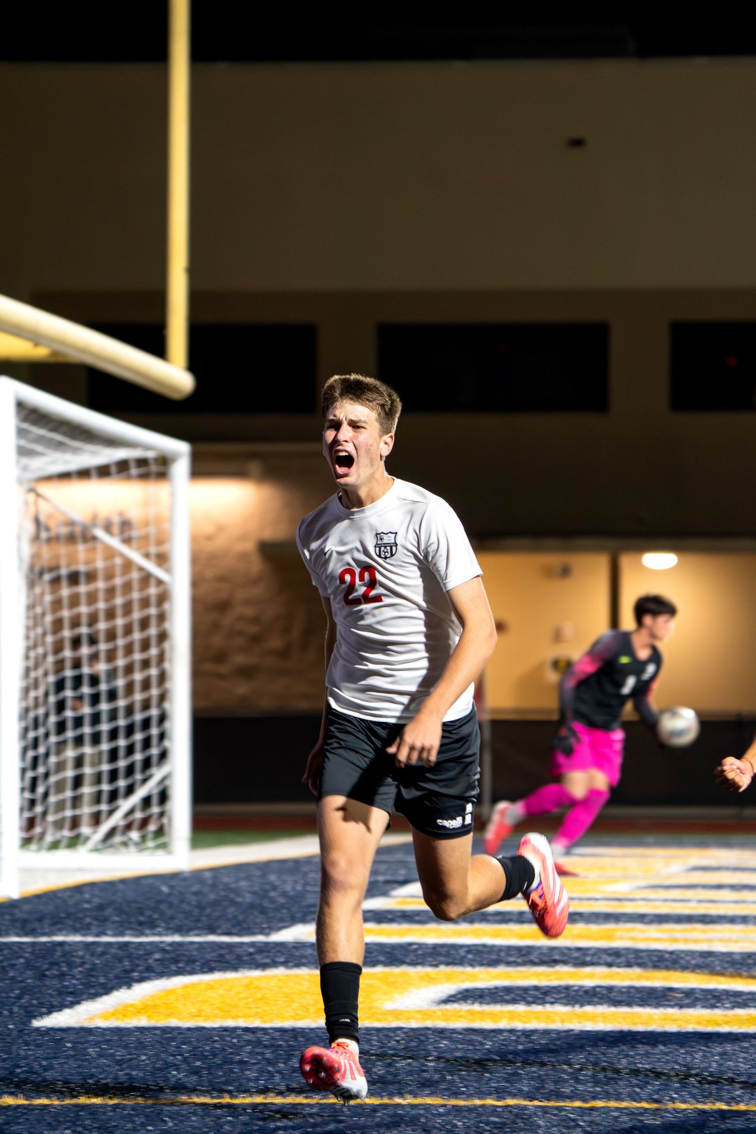Soccer player celebrating goal on field at night with stadium lights illuminating the scene.