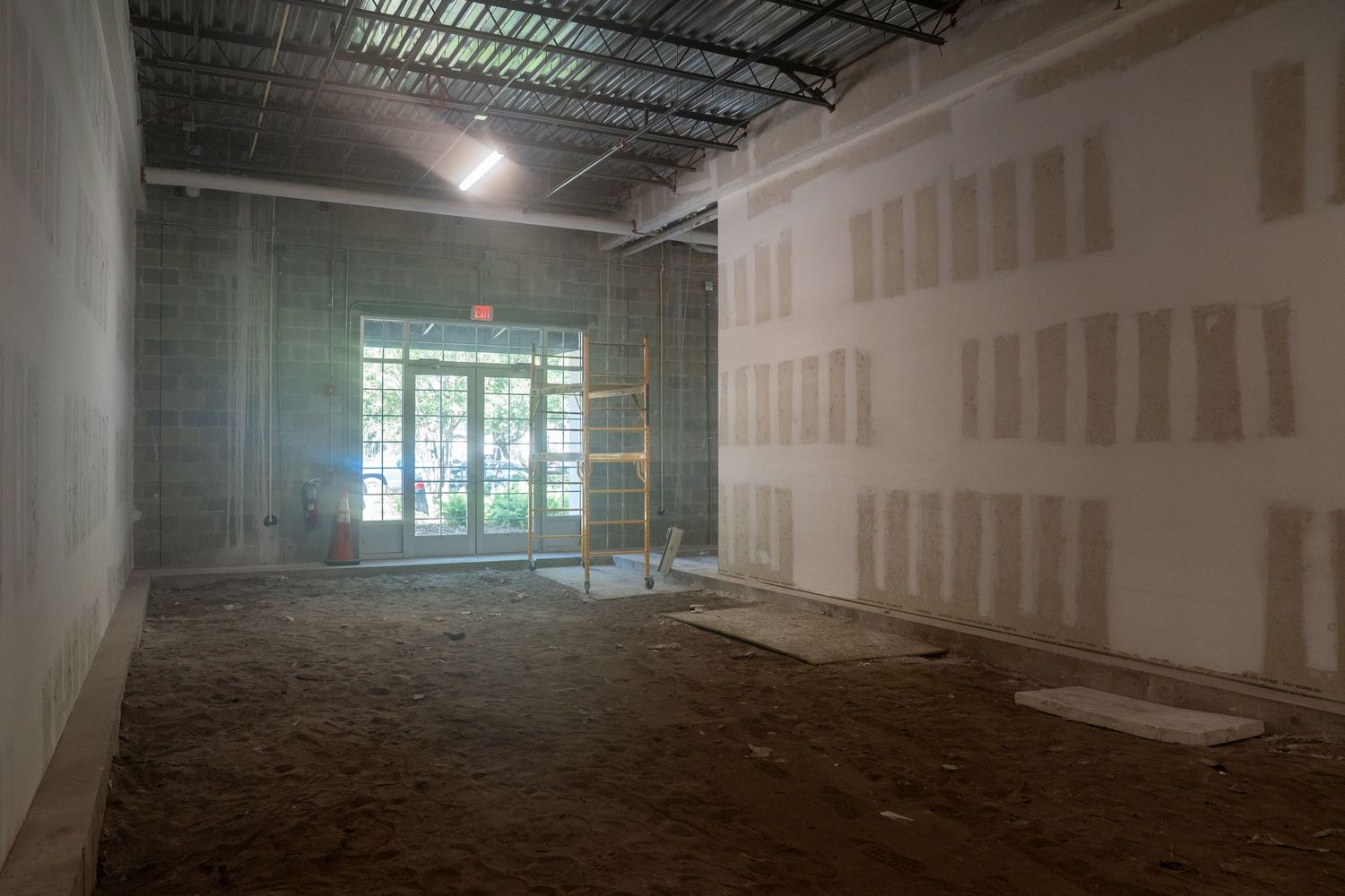 Unfinished commercial space with large windows and drywall walls during renovation.