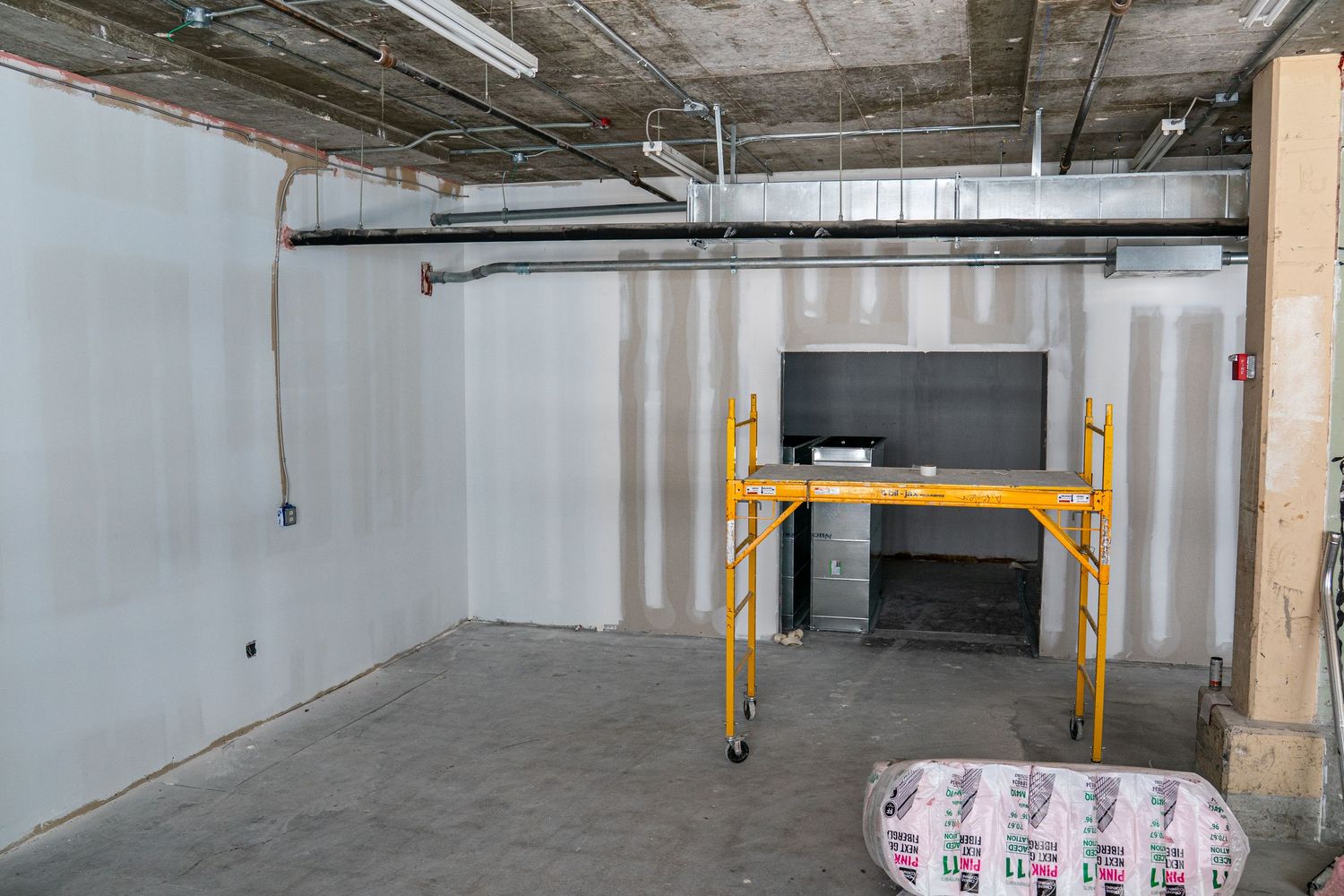 Panoramic view of empty commercial space with white walls and industrial ceiling.