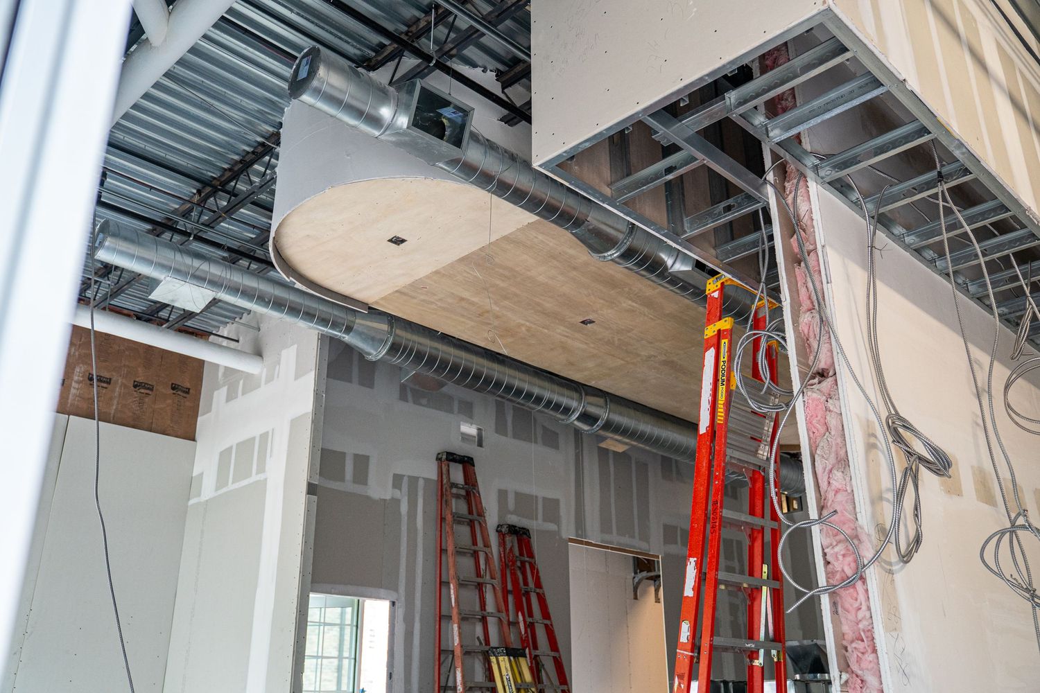Construction site interior showing white drywall installation and exposed industrial ceiling.