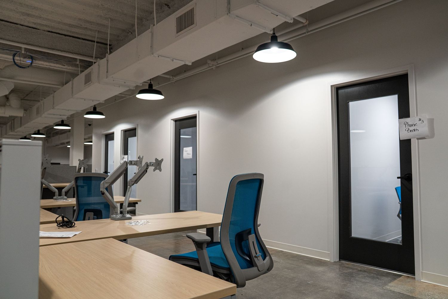 Industrial-style workspace with hanging pendant lights and blue office chairs along desks.