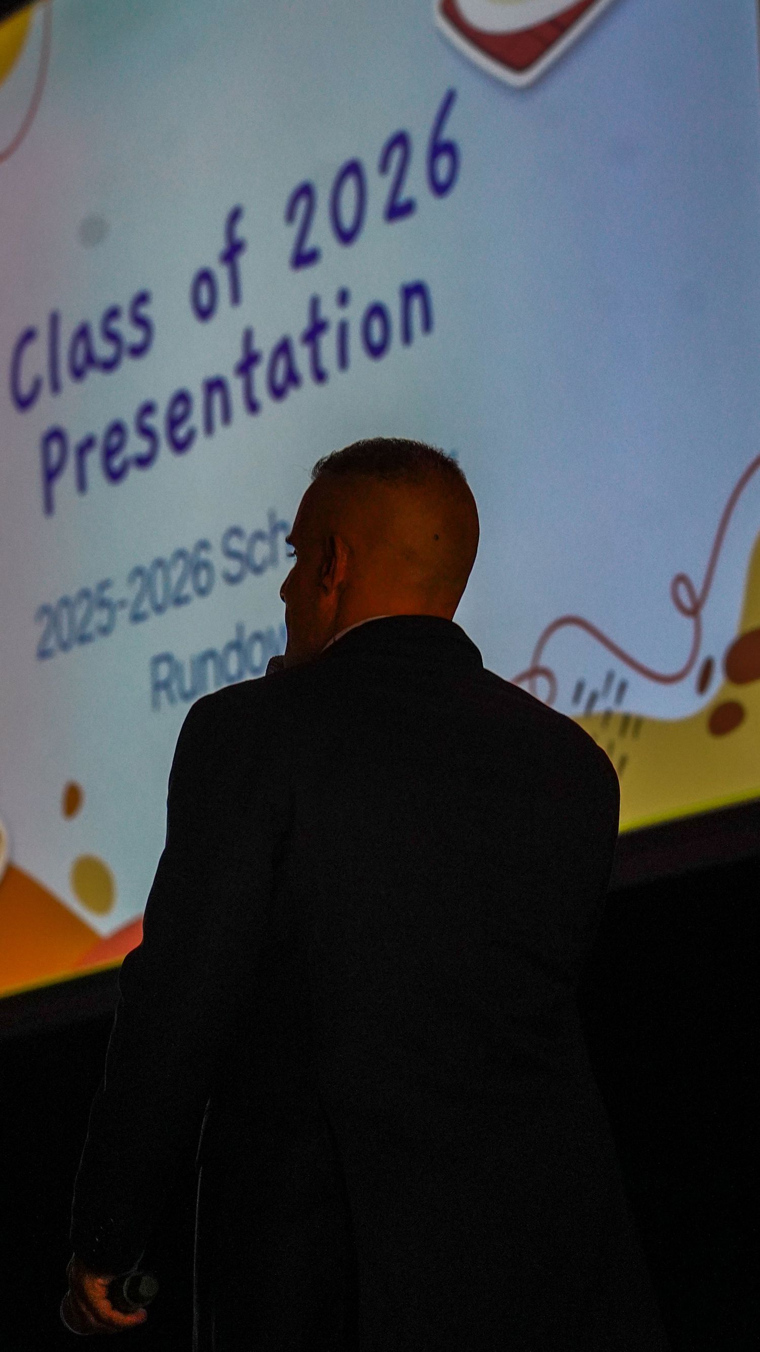 A dark silhouette against a colorful presentation screen displaying text and graphics.