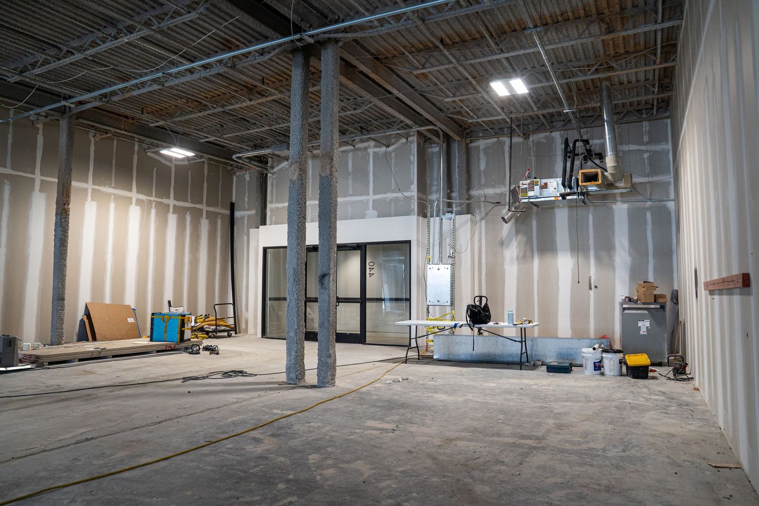 Wide industrial space under construction showing exposed beams and temporary lighting.