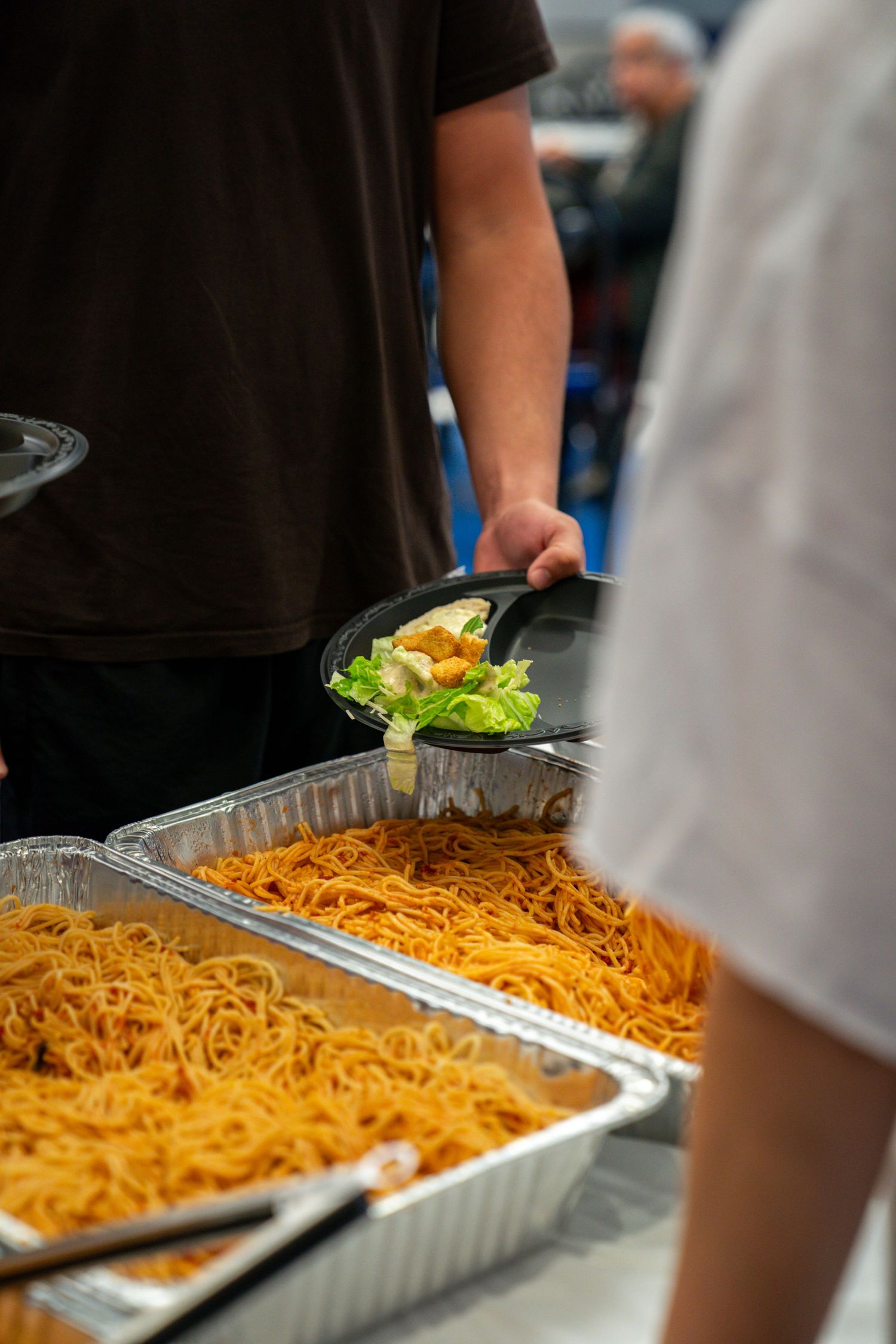 Close-up view of pasta being served from aluminum catering trays.