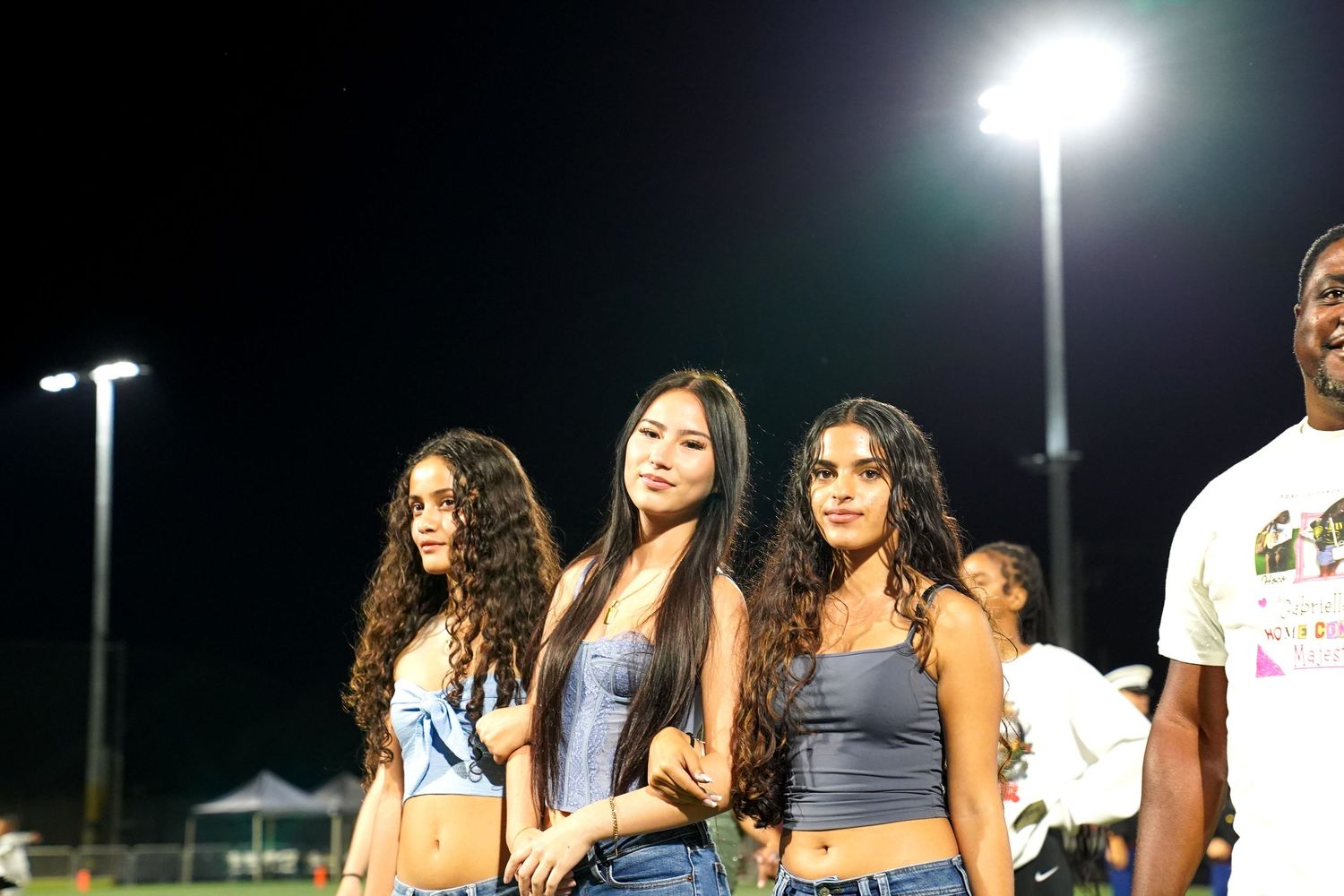 Students stand in formation on a sports field during a nighttime outdoor ceremony.