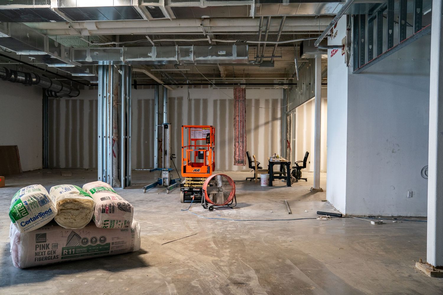 Construction site interior with building materials and equipment scattered on concrete floor.