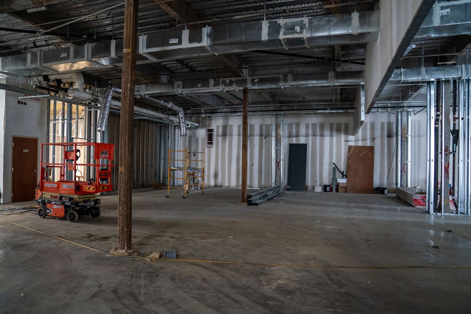 An unfinished commercial space with metal framing, exposed pipes, and construction equipment.