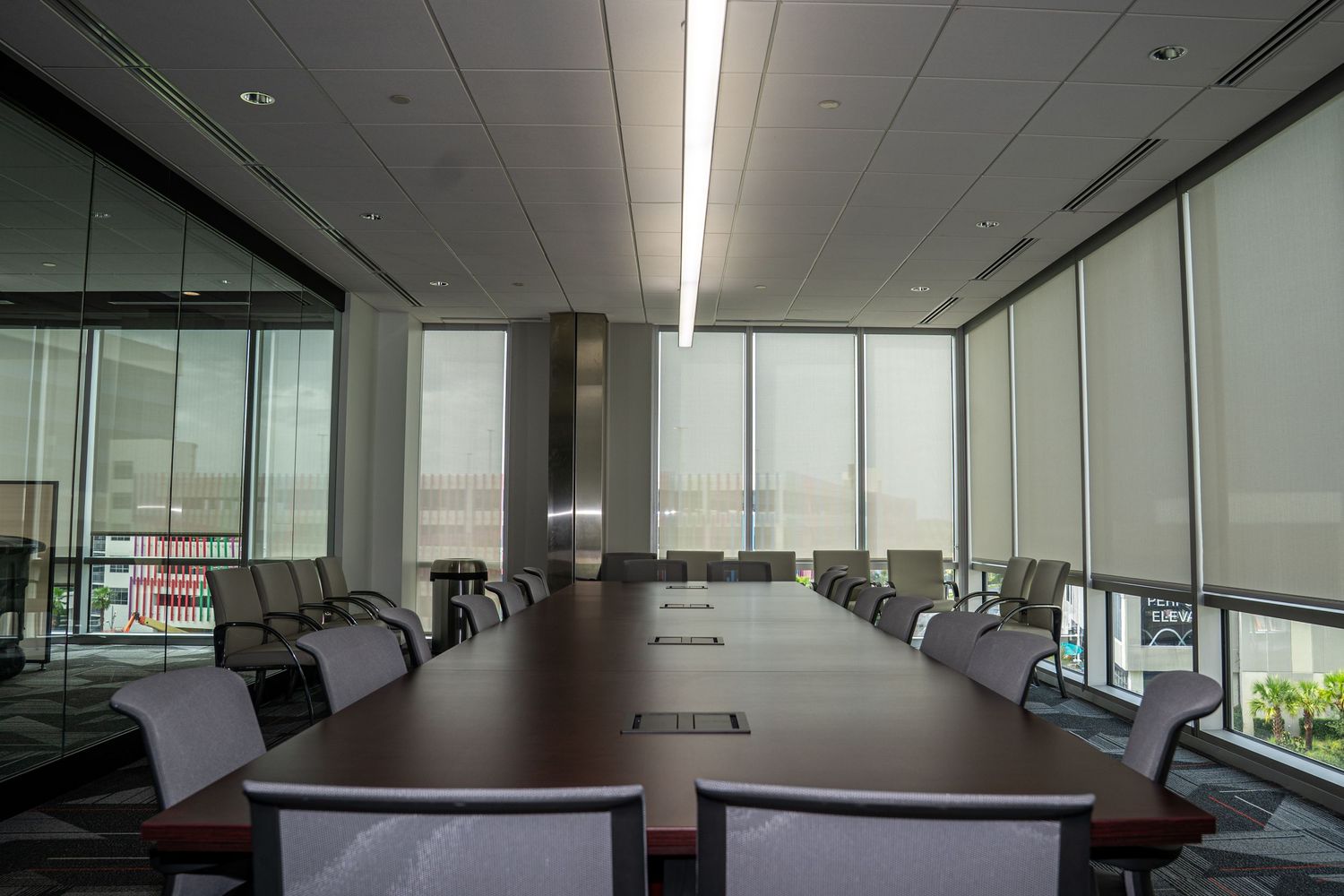 Modern boardroom featuring dark wood table, white chairs, and panoramic windows with city views.