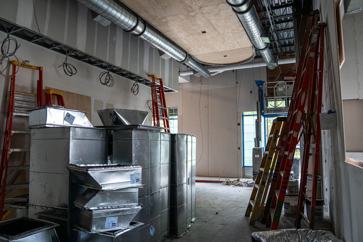 Industrial space under construction with metal ductwork and orange ladders against white walls.