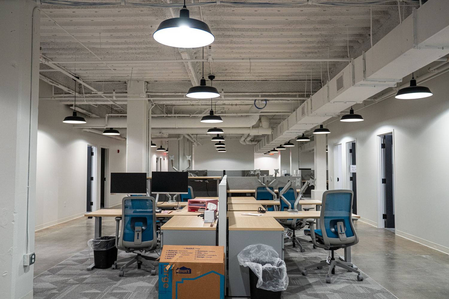 Large commercial office space with industrial ceiling, workstations, and blue ergonomic chairs.