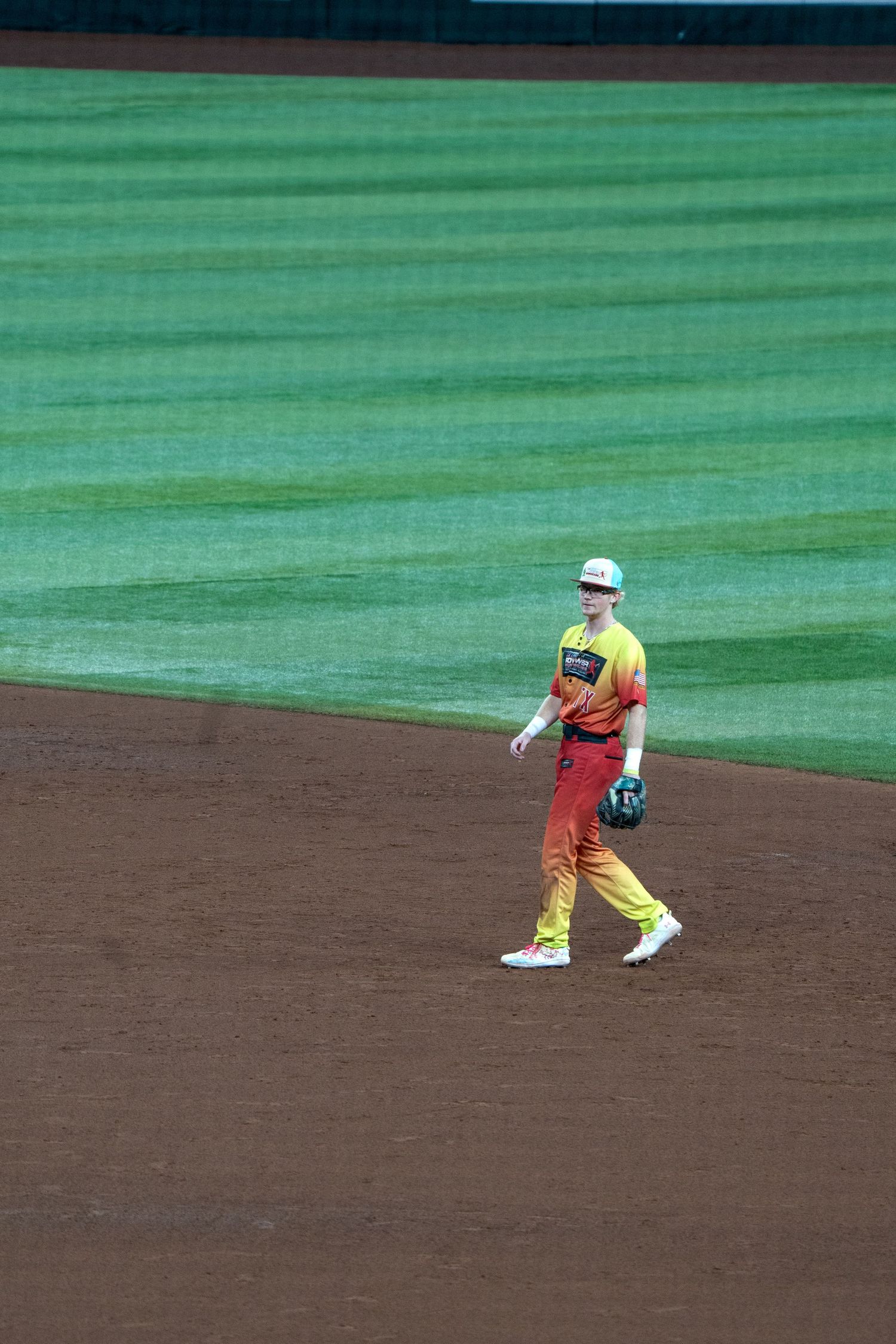 A baseball player in a yellow uniform crouches in a fielding position on the infield dirt.