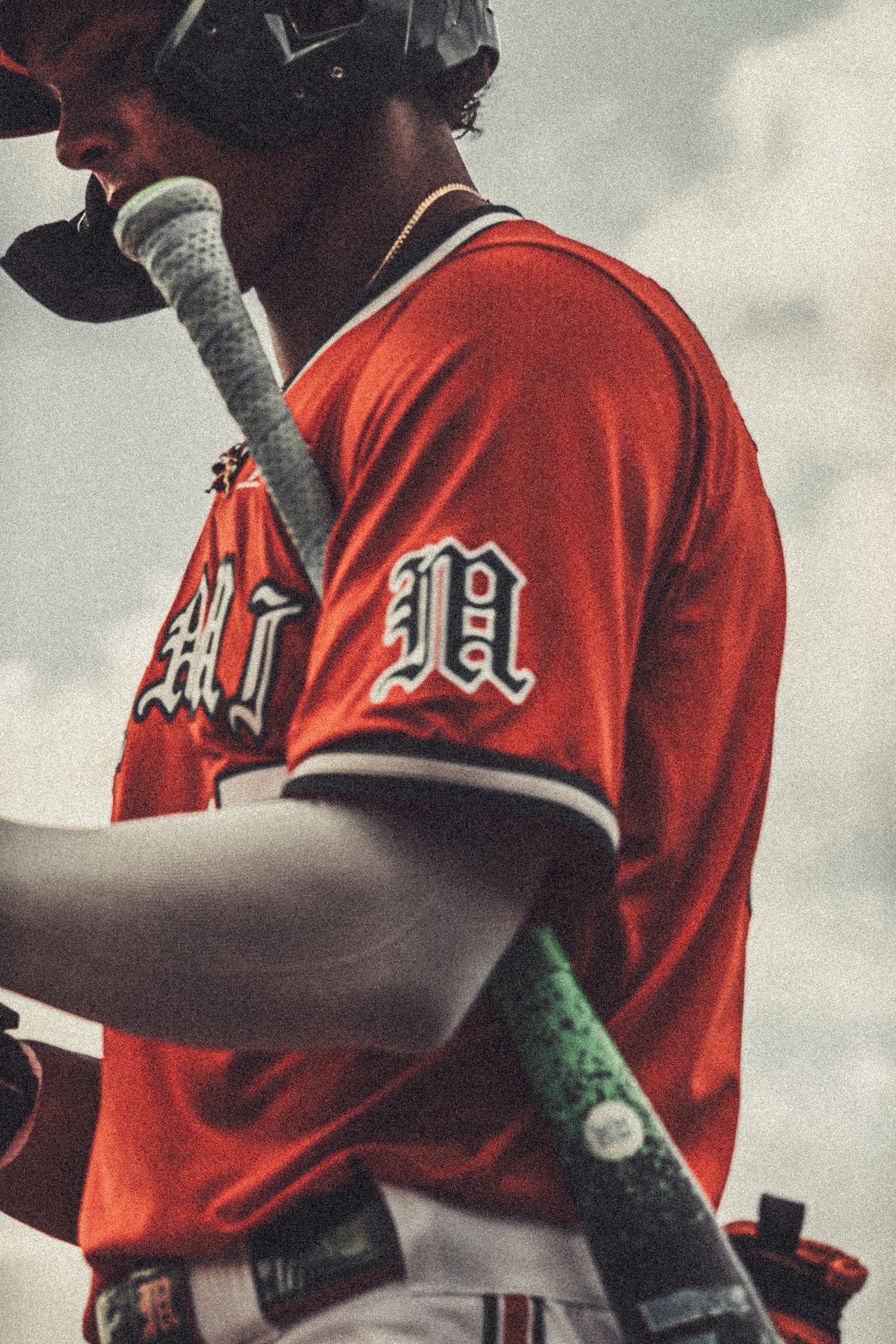 Baseball player in red Miami jersey holding a bat, photographed from behind in dramatic overcast lighting.